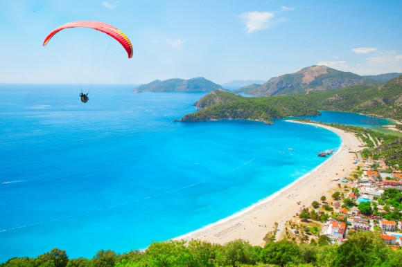 The Blue Lagoon in Oludeniz Turkey and its green landscapes and sweeping sun-drenched coast. Featuring parasailing on a hot day.