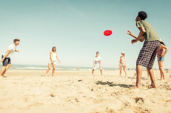 A group playing with a red frisbee on the beach.