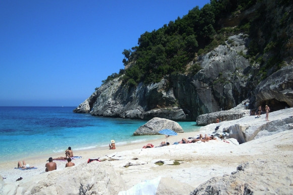 The beautiful white sand beach of Cala Goloritze in Sardinia Italy. Holidaymakers are sunbathing on the soft grains on a sunny day!