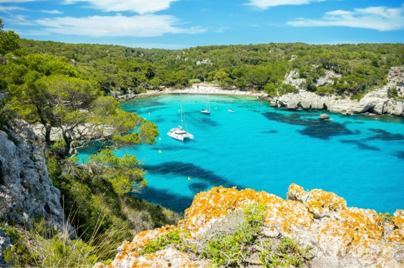 Sky view of the green surrounding landscape of Cala Macerell beach in Menorca and its gorgeous sun-soaked sands and sapphire Mediterranean waters.