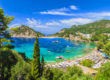 The breathtaking Palaiokastritsa Beach on the island of Corfu, surrounded by vast greenery and lined with sunloungers