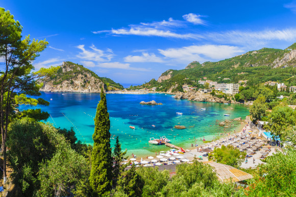 The breathtaking Palaiokastritsa Beach on the island of Corfu, surrounded by vast greenery and lined with sunloungers