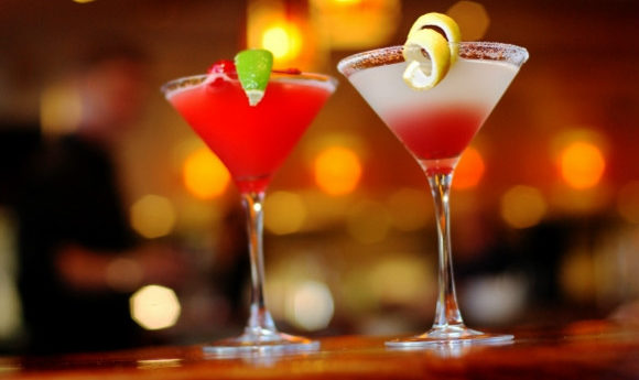 Two red martini-style cocktails accessorised with lemon and lime on a bar top.