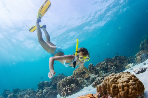 Woman snorkelling the coral reef floor in Greece with fishes floating in the background