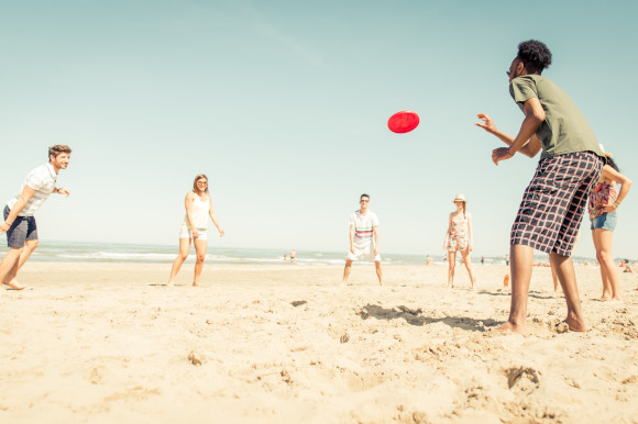 A group of friends playing with a red frisbee on the sand with the ocean behind them
