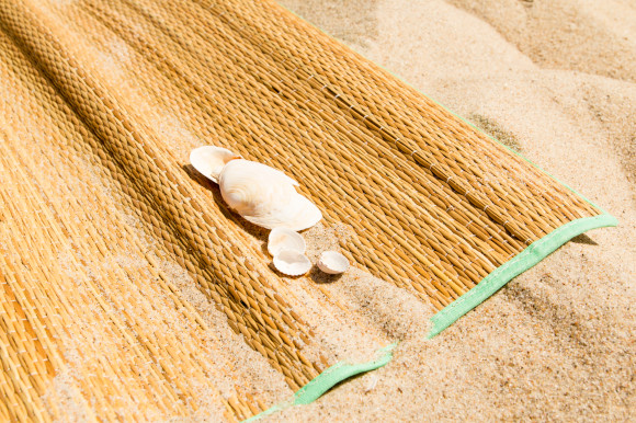Straw beach mat placed on the sand with shells on top