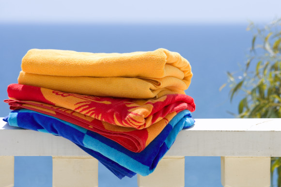 A pile of colourful beach towels placed on a white ledge with the sea in the background