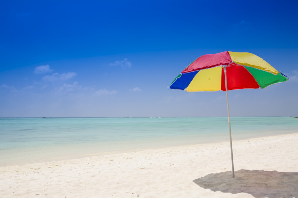 Multi-coloured beach umbrella dug into the sand on a beautiful beach with white sand and tranquil waters