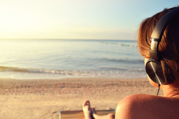 Woman wearing headphones on the beach with a view of the sun-lit ocean