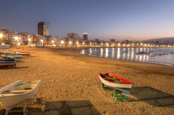 A night view of Las Canteras, near Las Palmas in Gran Canaria with fishing boats sitting on he sand and lit-up buildings in the background