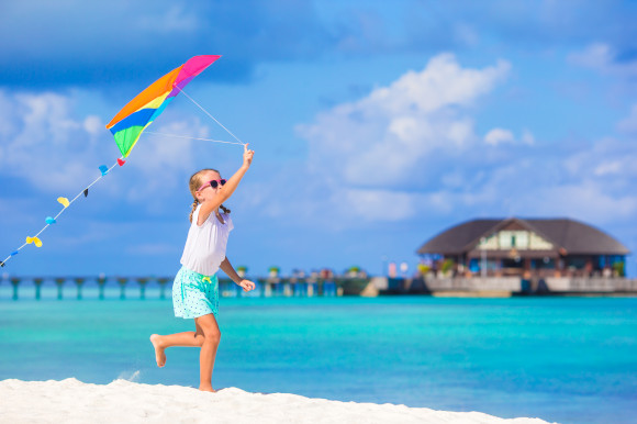 Little girl flying a colourful kite on an exotic beach with the ocean surrounding her