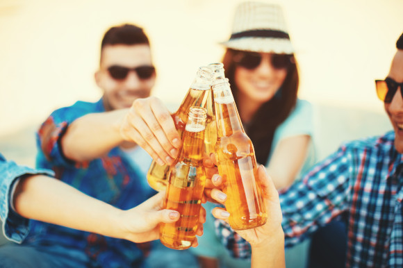 Young group of people drinking on the beach and clinking their bottles together