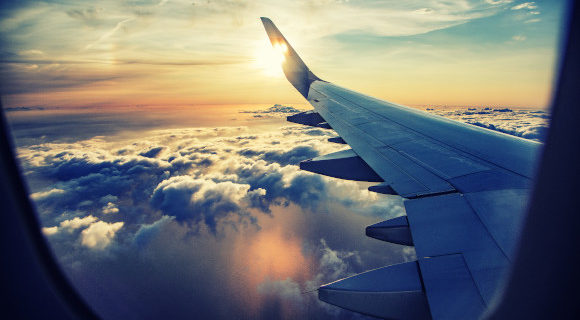 Views of the aeroplane wing and puffy white clouds from the plane window.