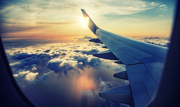 Views of the aeroplane wing and puffy white clouds from the plane window.