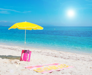 Yellow umbrella and towel placed on the sand with a beautiful beach backdrop featuring azure waters and a blue cloudless sky