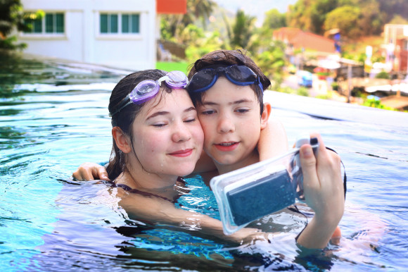 Two children in a swimming pool posing for a photo using a waterproof phone case