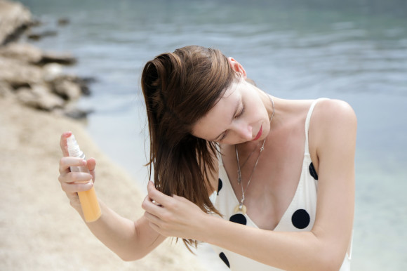 Woman in polka dot swimsuit using protection spray on the beach
