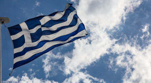 A waving Greek flag positioned against a bright blue sky
