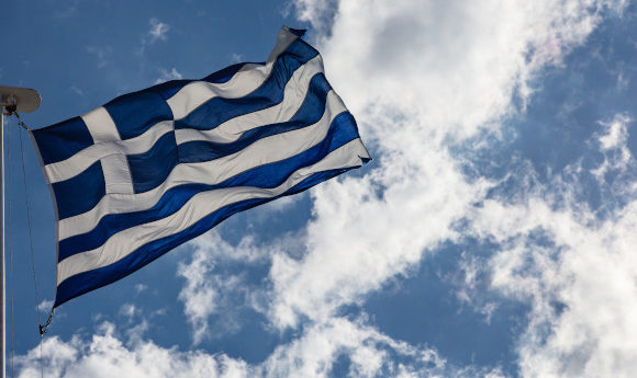 A waving Greek flag positioned against a bright blue sky