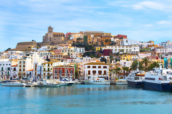 A view of the iconic Ibiza Town with whitewashed buildings overlooking the sea and luxury yachts 