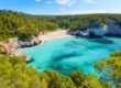 A view of the striking Mitjaneta Beach on the island of Menorca in Spain with shimmering turquoise waters and greenery