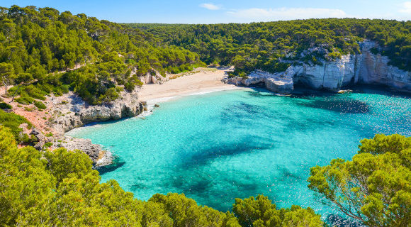 A view of the striking Mitjaneta Beach on the island of Menorca in Spain with shimmering turquoise waters and greenery