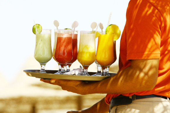 A waiter holding a tray of All Inclusive cocktails with a beach in the background