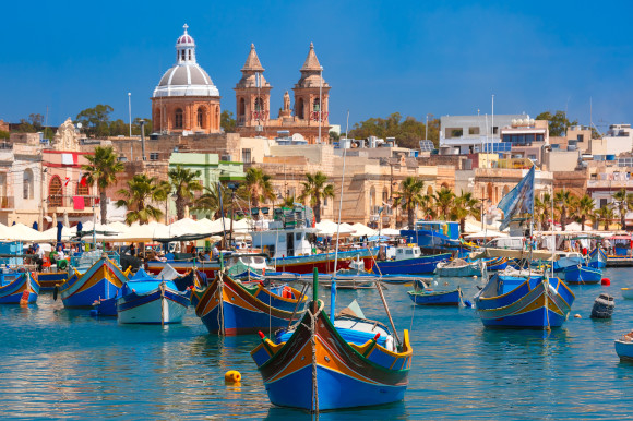 Brightly painted boats and sand coloured buildings in a fishing village, Malta