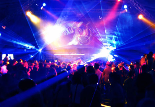 Neon blue, yellow and pink stobe lights flashing at a club with people dancing to the music