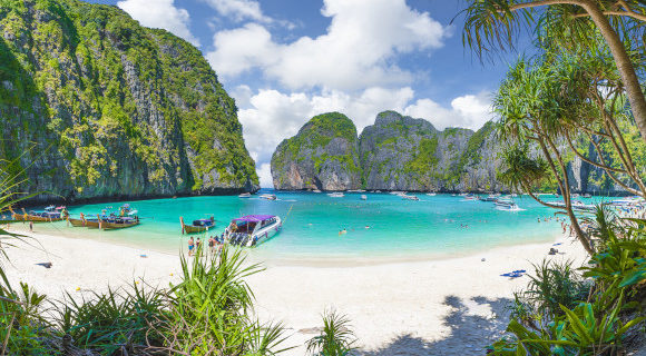 The famous Maya Bay in Thailand's popular Phi Phi Islands with long tail boats in the water and striking white sand