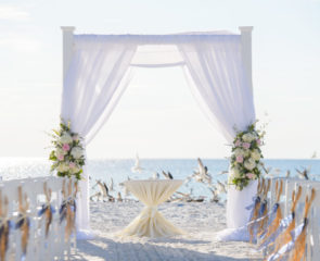 Beautiful white beach wedding on the shores of Spain with decorated white chairs and flowered walkway