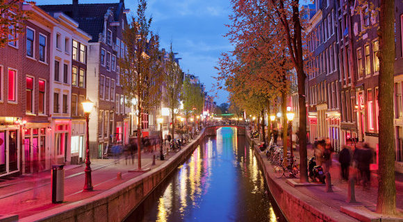 A beautiful view of Amsterdam at dusk showing a canal surrounded by grand buildings and trees