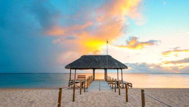 An amazing sunset in Mauritius with white sands surrounding a jetty and the sea sitting in the distance