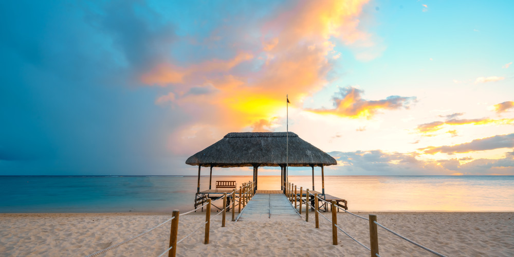 An amazing sunset in Mauritius with white sands surrounding a jetty and the sea sitting in the distance