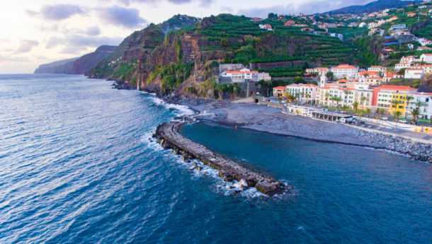 The sun setting below Madeira island with the Atlantic Ocean and orange roofed houses in the background