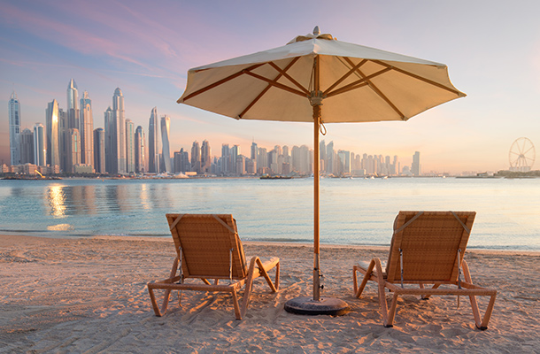 Beach in Dubai with two sun loungers and parasols with the city in the far distance