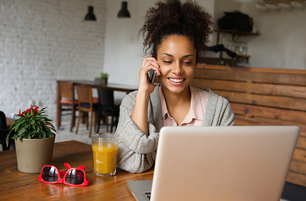 Woman on mobile phone looking at laptop planning a holiday